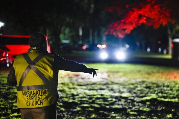 In this Sunday, Nov. 3, 2019, photo, Plains Mayor Boze Godwin directs cars into a pecan grove to park behind Maranatha Baptist Church before dawn, in Plains, Ga. Guests begin arriving the day before to attend the Sunday school class that former President Jimmy Carter teaches. (AP Photo/John Amis)
