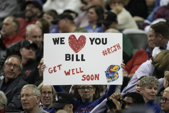 A fan holds up a get well sign for Kansas head coach Bill Self during the first half of an NCAA college basketball game against West Virginia in the second round of the Big 12 Conference tournament Thursday, March 9, 2023, in Kansas City, Mo. Self was not at the game after being hospitalized. (AP Photo/Charlie Riedel)