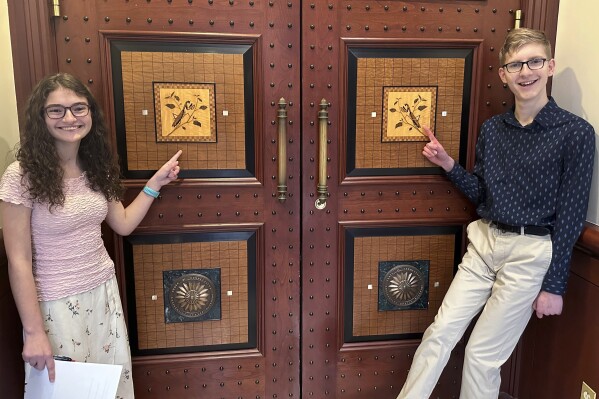 Sue Katherine Boye Williams, 16, a junior at the Watkinson School in Hartford, Conn. and Chris Tracy, 19, a senior at the school, stand near an inlaid design of Connecticut's current State Insect, the European "Praying" Mantis, on the door to a hearing room at Connecticut's Legislative Office Building in Hartford on March 8, 2024. Both testified before a legislative committee, urging lawmakers to replace the non-native praying mantis with the native Spring Azure Butterfly. (AP Photo/Susan Haigh)