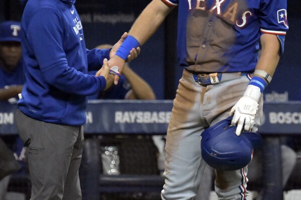 A Texas Rangers trainer, left, looks over Josh Jung after he was hit by a foul ball against the Tampa Bay Rays during the ninth inning of a baseball game Monday, April 1, 2024, in St. Petersburg, Fla. Jung left the game and was replaced by a pinch hitter. (AP Photo/Steve Nesius)