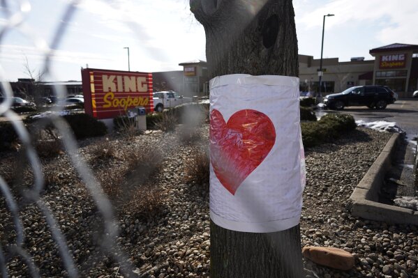 A drawig of a heart is wrapped on a tree behind the makeshift fence put up around the parking lot outside a King Soopers grocery store where a mass shooting took place Tuesday, March 23, 2021, in Boulder, Colo. (AP Photo/David Zalubowski)