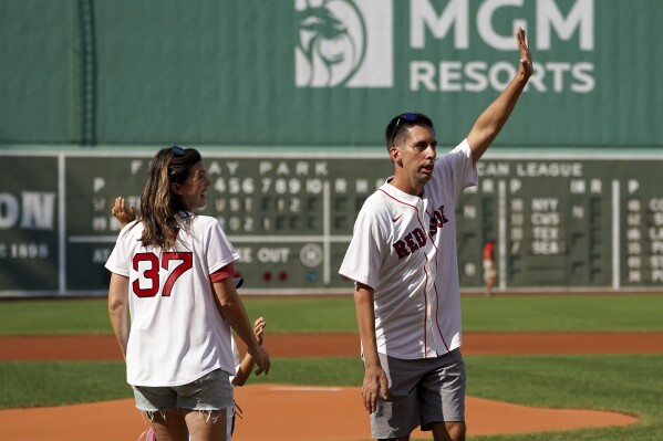 FILE - Chris Snow, an assistant general manager for the Calgary Flames NHL hockey team, waves to the fans as his wife, Kelsie, looks on before throwing out a ceremonial first pitch before a baseball game between the Boston Red Sox and Tampa Bay Rays at Fenway Park, Thursday, Aug. 12, 2021, in Boston. On Saturday, Sept. 30, 2023, the Flames confirmed that Snow has died after a lengthy public battle with Lou Gehrig's disease. He was 42. (AP Photo/Mary Schwalm, File)