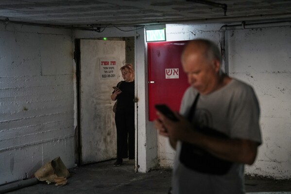 Residents check their cell phones at a shelter during an alarm for incoming missiles launched from Iran in Haifa, Israel, Sunday, June 22, 2025. (AP Photo/Baz Ratner)