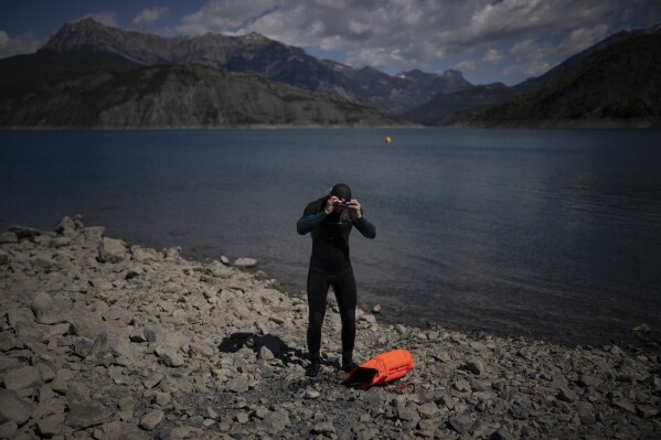 A swimmer dries off after traversing a section of the Serre-Poncon resevoir in France, Tuesday, May 2, 2023. Human-caused climate change is lengthening droughts in southern France, meaning the reservoirs are increasingly drained to lower levels to maintain the power generation and water supply needed for nearby towns and cities. It's concerning those in the tourism industry, who are working out how to keep their lakeside businesses afloat. (AP Photo/Daniel Cole)