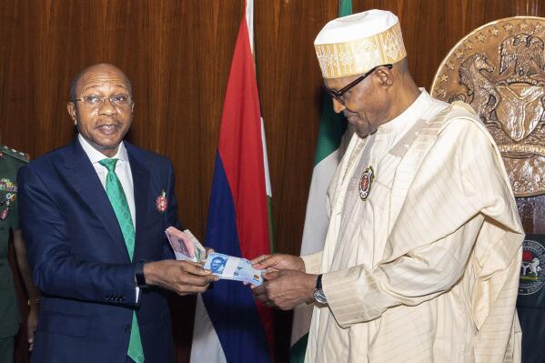 In this photo released by the Nigeria State House, Nigeria's central bank governor, Godwin Emefile, left, presents the newly designed currency notes to Nigeria's President Muhammadu Buhari, right, during a launch in Abuja, Nigeria, Tuesday, Nov. 22, 2022. Nigeria has unveiled newly designed currency notes that the West African nation’s central bank says will help curb inflation and money laundering. (Sunday Aghaeze/Nigeria State House via AP)