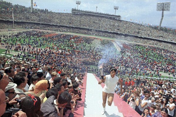 FIK]LE - In this Oct. 12, 1968, file photo, Mexican hurdler Enriqueta Basilio, the first woman to make the final run of the torch and to light the Olympic flame, carries the Olympic torch up the 90 steps to the Olympic flame cauldron in the Olympic Stadium during opening ceremonies for the Olympic Games in Mexico City. (AP Photo/File)