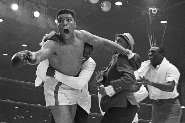 Cassius Clay's handlers hold him back as he reacts after he is announced the new heavyweight champion of the world on a seventh round technical knockout against Sonny Liston at Convention Hall in Miami Beach, Fla., on Feb. 25, 1964.  (AP Photo)