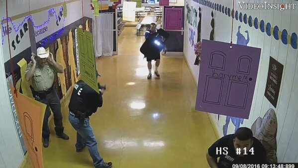 In this still frame image taken from video provided by the Texas Rangers and recorded on Sept. 8, 2016, armed law enforcement officers move through a hallway at Alpine High School in Alpine, Texas, while responding to a shooting at the school. A Homeland Security Investigations Special Agent was wounded during the response after a gun carried by U.S. Marshal Douglas Mullens, upper-right, accidentally discharged. (Courtesy of Texas Rangers via AP)