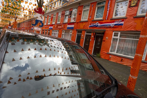 Orange tarp, orange bunting, and Dutch national flags are reflected un a car windscreen as they decorate Marktweg street in The Hague, Netherlands, Thursday June 13, 2024, one day ahead of the start of the Euro 2024 Soccer Championship. (AP Photo/Peter Dejong)