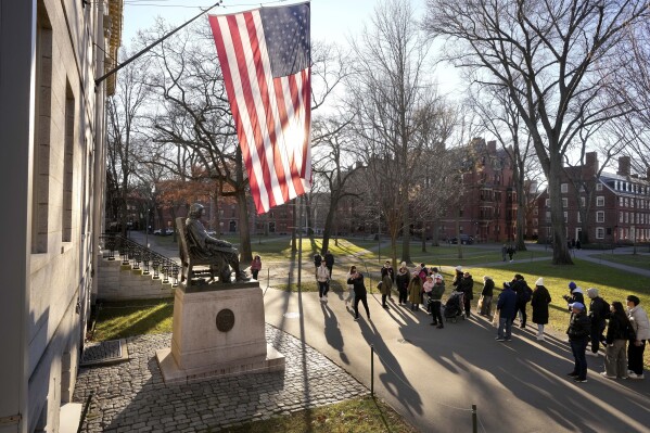 People take photographs near a John Harvard statue, left, Tuesday, Jan. 2, 2024, on the campus of Harvard University, in Cambridge, Mass. Harvard University President Claudine Gay resigned Tuesday amid plagiarism accusations and criticism over testimony at a congressional hearing where she was unable to say unequivocally that calls on campus for the genocide of Jews would violate the school's conduct policy. (AP Photo/Steven Senne)