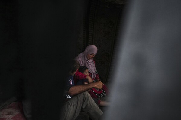 Basima al-Batsh sits with her family ahead of the Eid al-Adha holiday in Deir al Balah، Gaza Strip، Tuesday، June 11، 2024. They were displaced from their home by the war between Israel and Hamas. (AP Photo/Abdel Kareem Hana)