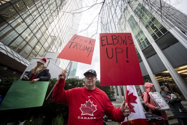A demonstrator holds up signs during a protest outside of the U.S embassy in Vancouver, British Columbia, Tuesday, March 4, 2025. (Ethan Cairns/The Canadian Press via AP)