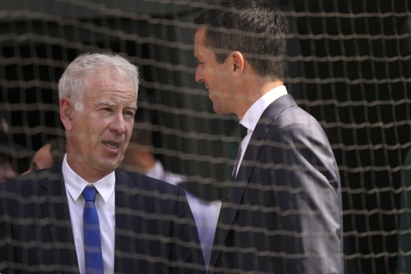 FILE - Tennis legend John McEnroe, left, speaks to former British tennis player Tim Henman on Centre Court, July 7, 2023, on day five of the Wimbledon tennis championships in London. McEnroe has COVID-19 and so is missing time as ESPN's lead tennis analyst on its coverage of its U.S. Open television coverage. “Unfortunately, after feeling a bit under the weather, I tested positive for COVID," McEnroe said in a statement released by the network on Tuesday, Aug. 29, the second day of the Grand Slam tournament. (AP Photo/Alberto Pezzali, File)