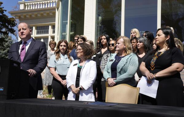 Colorado Governor Jared Polis speaks before signing into law the reproductive health equity act during a ceremony outside the governor's mansion, Monday, April 4, 2022, in Denver. The bill's sponsors, Sen. Julie Gonzalez, far right, Rep. Meg Froelich, center, and House majority leader Daneya Esgar, look on with guests and other lawmakers at the signing. (AP Photo/David Zalubowski)