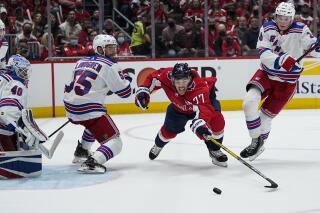 Washington Capitals right wing T.J. Oshie (77) reaches for the puck from between New York Rangers defenseman Ryan Lindgren, left, and right wing Kaapo Kakko (24) during the first period of an NHL hockey game Wednesday, Oct. 13, 2021, in Washington. (AP Photo/Alex Brandon)