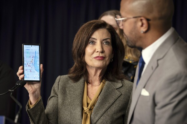 New York Gov. Kathy Hochul holds up a phone that displays a map of illegal cannabis stores as entrepreneur Alfredo Angueira looks on during a press conference, Wednesday, Feb. 28, 2024 in New York. Unable to reign in illegal cannabis shops in New York, the state's governor is asking digital mapping and search companies to hide or relabel the many illegal shops. (AP Photo/Stefan Jeremiah)