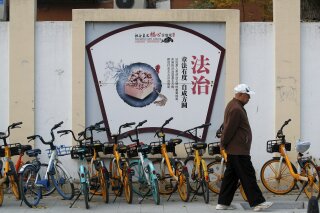 A man walks by a propaganda board depicting China's legal system promoting the government's socialist core values near residential buildings in Beijing, Wednesday, Nov. 11, 2020. A prominent Chines...