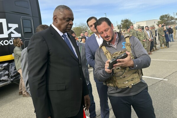 Defense Secretary Lloyd Austin takes a closer look at the device used to control a swarm of drones that lifted off from a parking area at the Defense Innovation Unit in Mountain View, Calif, on Friday, Dec. 1, 2023. Austin is in California for meeting with defense ministers from Australia and the United Kingdom, but took some time to see several projects under development at DIU. (AP Photo/Lolita Baldor)