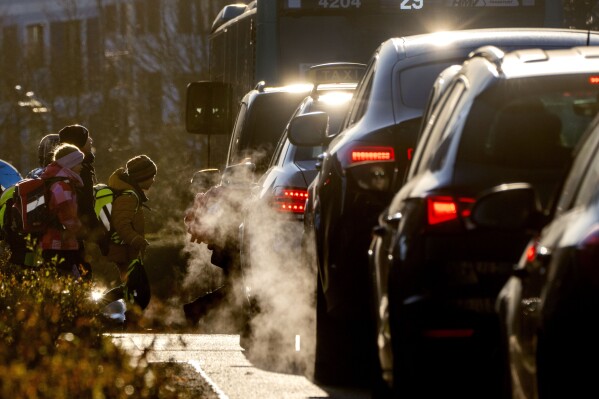 FILE - Cars release exhaust fumes as children head to school in Frankfurt, Germany, Feb. 27, 2023. European Union member countries have watered down a proposal by the bloc's executive arm aimed at lowering vehicle emissions. The European Commission had proposed last year updated pollution standards for new combustion engine vehicles that are expected to remain on European roads well after the 27-nation bloc bans their sale in 2035, with the aim of lowering emissions from tailpipes, brakes and tires. (AP Photo/Michael Probst, File)