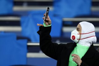 A fan wearing a protective mask takes a picture with her cell phone prior the Champions League, round of 16, first leg soccer match between Real Madrid and Manchester City at the Santiago Bernabeu stadium in Madrid, Spain, Wednesday, Feb. 26, 2020. (AP Photo/Manu Fernandez)