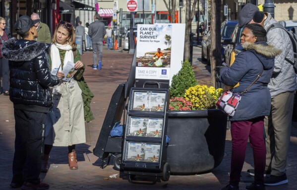 A woman shares Jehovah's Witnesses' literature with a passerby in downtown Pittsburgh on Monday, Nov. 13, 2023. Jehovah's Witnesses regularly distribute literature in public places and do door-to-door evangelism, but for the first time in more than a century, their congregations will not be regularly tracking their hours in ministry. (AP Photo/Peter Smith)