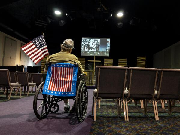 A man in a wheelchair watches a live video feed during the ReAwaken America Tour from inside the Cornerstone Church in Batavia, N.Y., Friday, Aug. 12, 2022. (AP Photo/Carolyn Kaster)
