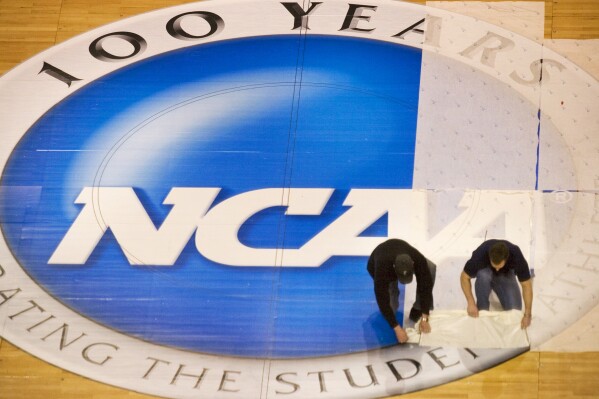FILE - Wachovia Center operations manager Jim McDonald, left, and carpenter foreman Tim Allen remove the protective film covering the NCAA logo at mid-court on the center's basketball court, Wednesday, March 15, 2006, in Philadelphia. NCAA athletes will be immediately eligible to play no matter how many times they transfer — as long as they meet academic requirements — after the association fast-tracked legislation Wednesday, April 17, 2024, to fall in line with a recent court order. (Ed Hille/The Philadelphia Inquirer via AP, FIie)