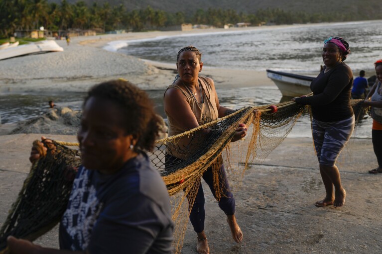 Fisherwoman Greyla Aguilera and coworkers carry a net to place it on the beach on the coast of Chuao, Venezuela, Thursday, June 8, 2023. Aguilera, 48, said fisherwomen rely on each other and their parents to care for their children while they are at sea. "Someone always steps up to ensure that no woman misses a fishing shift," she said. (AP Photo/Matias Delacroix)