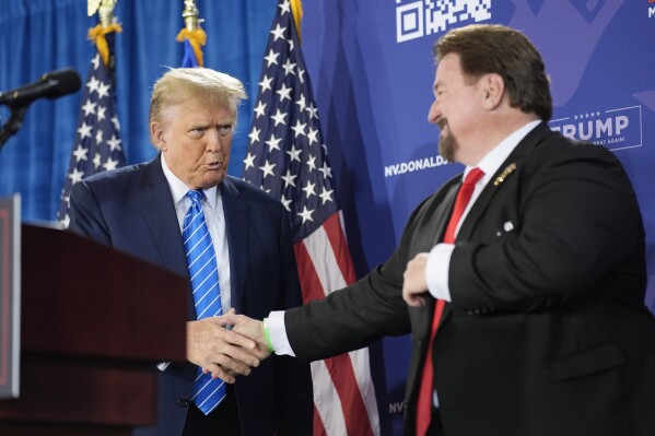 FILE - Nevada GOP chair Michael McDonald, right, shakes hands with Republican presidential candidate former President Donald Trump at a campaign event, Jan. 27, 2024, in Las Vegas. Six Republicans accused of falsely declaring Donald Trump the winner of Nevada’s 2020 presidential election will not stand trial until sometime next year. A Nevada judge on Monday, March 4, 2024 pushed back the trial date due to conflicting schedules. The judge also set an April 22 hearing on a bid by McDonald and other defendants to throw out the indictment. (AP Photo/John Locher, File)
