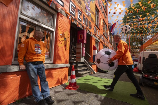 Volunteers carry inflatable soccer balls as orange tarp, orange bunting, and Dutch national flags decorate Marktweg street in The Hague, Netherlands, Thursday June 13, 2024, one day ahead of the start of the Euro 2024 Soccer Championship. (AP Photo/Peter Dejong)