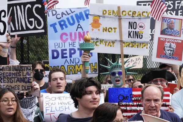 Demonstrators carrying signs stand near the White House during a protest taking place on the day of a military parade commemorating the Army's 250th anniversary, coinciding with President Donald Trump's 79th birthday, Saturday, June 14, 2025, in Washington. (AP Photo/Alex Brandon)