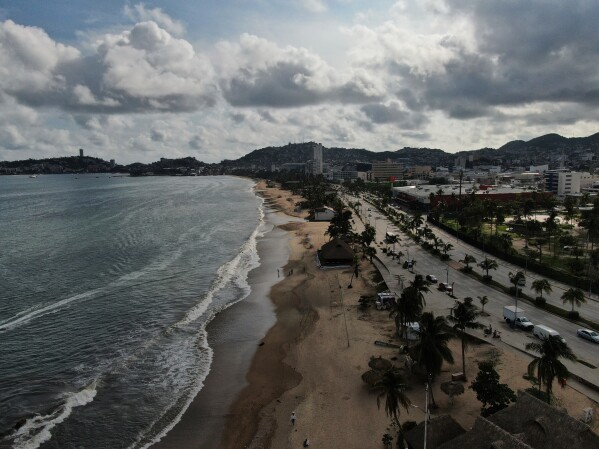 Turistas caminham na beira da praia antes da chegada do Furacão Erick, em Acapulco, México.