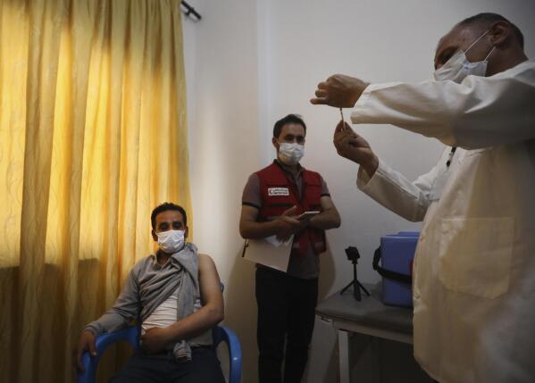 A Syrian health staff, right, prepares a shot of AstraZeneca COVID-19 vaccine to be given for a man, left, at Ibn Sina Hospital, in Idlib town, northwestern Syria, Saturday, May 1, 2021. The inoculation campaign against COVID-19 kicked off in Syria's last rebel-held enclave in the country's northwest, with a 45-year-old front line nurse becoming the first to receive the UN-secured Jabs on Saturday. (AP Photo/Ghaith Alsayed)