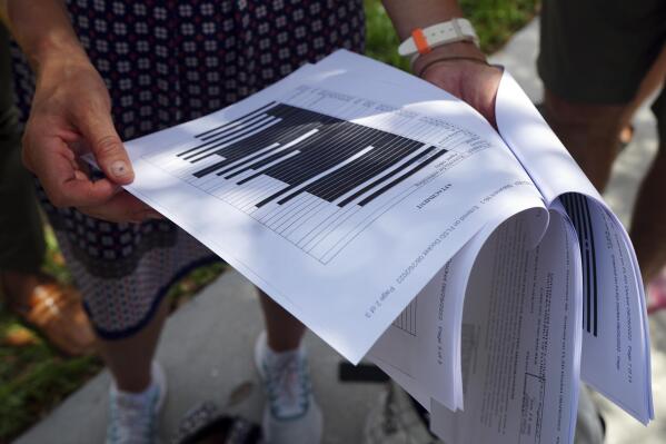 Journalists gather outside the Paul S. Rogers Federal Building and U.S. Courthouse in downtown West Palm Beach, Fla., to read a heavily blackout document released by The Justice Department Friday, Aug. 26, 2022.  The 32-page affidavit, even in its heavily redacted form, offers the most detailed description to date of the government records being stored at former President Donald Trump's Mar-a-Lago property long after he left the White House and reveals the gravity of the government's concerns that the documents were there illegally. (AP Photo/Jim Rassol)