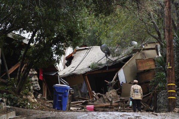 A local resident checks the damage to her neighbor's house after heavy rains and mud flows caused it to slide down from the hill in the Beverly Glen section of Los Angeles on Wednesday, Feb. 7, 2024. A storm that parked itself over Southern California for days, unleashing historic downpours that caused hundreds of landslides, was moving out of the region after one final drenching Wednesday, but authorities warned of the continued threat of collapsing hillsides. (APPhoto/Richard Vogel)
