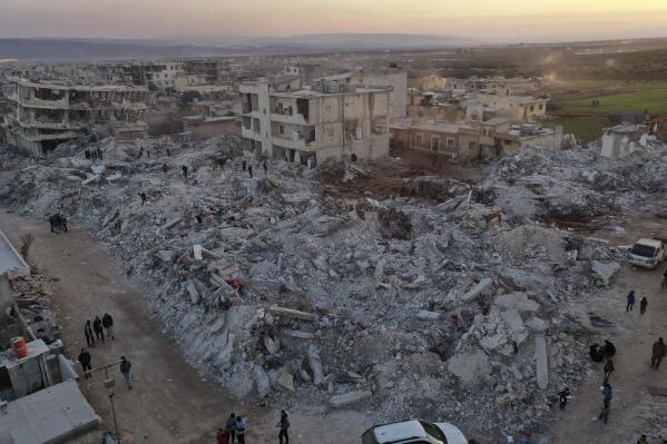 People walk past collapsed buildings following a devastating earthquake in the town of Jinderis, Aleppo province, Syria, Thursday, Feb. 9, 2023. The quake that razed thousands of buildings was one of the deadliest worldwide in more than a decade. (AP Photo/Ghaith Alsayed)