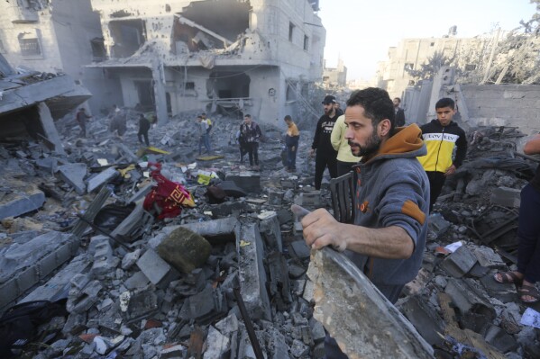 Palestinians stand by a building destroyed in Israeli bombardment overnight in Rafah, Gaza Strip, Friday, Nov. 24, 2023. (AP Photo/Hatem Ali)