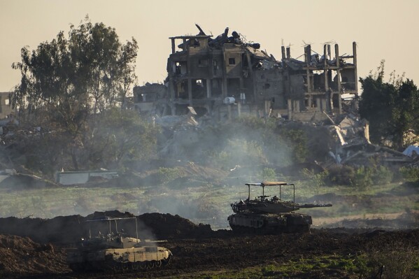 Israeli tanks are seen next to a destroyed building during a ground operation in the northern Gaza Strip, Friday, Dec. 15, 2023. The army is battling Palestinian militants across Gaza in the war ignited by Hamas' Oct. 7 attack on Israel. (AP Photo/Ariel Schalit)