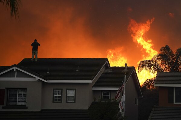 FILE - In this Tuesday, Oct. 27, 2020 file photo, Herman Termeer, 54, stands on the roof of his home as the Blue Ridge Fire burns along the hillside in Chino Hills, Calif. An overheating world obliterated weather records in 2020 — an extreme year for hurricanes, wildfires, heat waves, floods, droughts and ice melt — the United Nations’ weather agency reported Wednesday, Dec. 2, 2020. (AP Photo/Jae C. Hong)