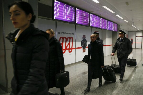 Flight crew members walk past the arrivals board with the cancelled flight from Tehran after Ukrainian 737-800 plane crashed on the outskirts of Tehran, Iran, at Borispil international airport outside Kyiv, Ukraine, Wednesday, Jan. 8, 2020. A Ukrainian airplane carrying 176 people crashed on Wednesday shortly after takeoff from Tehran's main airport, killing all onboard, Iranian state TV and officials in Ukraine said. (AP Photo/Efrem Lukatsky)