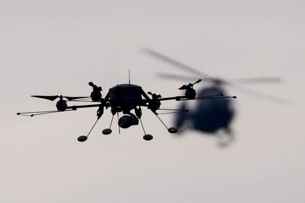 FILE - A drone, left, and Serbian Army Airbus H145M multi-utility helicopter fly during the military exercise at the army barracks in Pancevo, some 16 kilometers (10 miles) north of Belgrade, Serbia, Monday, Jan. 3, 2022. Serbia has received more arms deliveries from Russia despite international sanctions over Ukraine and claims by the Balkan country's leadership that they are seeking European Union membership. Serbian President Aleksandar Vucic on Wednesday presented a Russian anti-drone system for electronic jamming known as Repellent that he recently said 