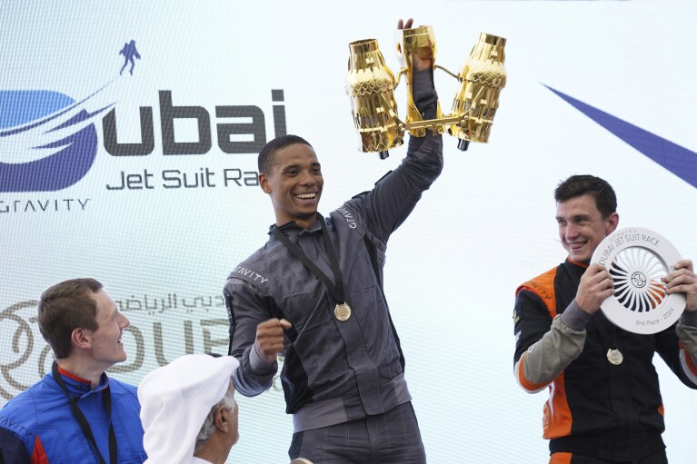 Jet suit pilot Issa Kalfon of the United Kingdom, center, waves his trophy after winning a race in Dubai, United Arab Emirates, Wednesday, Feb. 28, 2024. Dubai on Wednesday hosted what it called its first-ever jet suit race. Racers zipped along a route with the skyscrapers of Dubai Marina looming behind them, controlling the jet engines on their hands and their backs. (AP Photo/Jon Gambrell)
