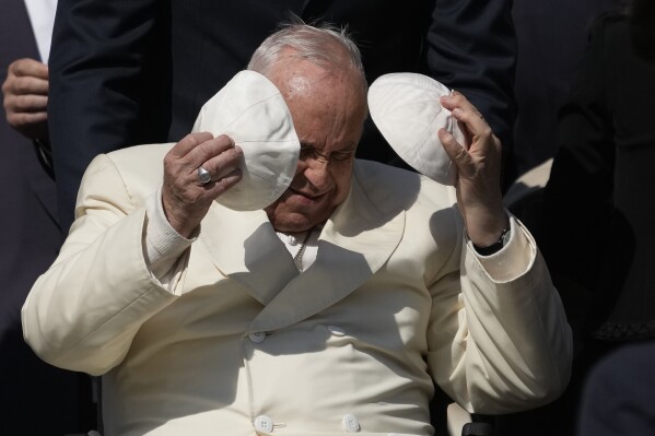 Pope Francis exchanges his skull cap with one presented by a participant in the weekly general audience in St. Peter's Square, at the Vatican, April 19, 2023. (AP Photo/Alessandra Tarantino)