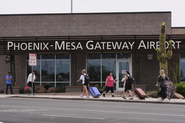 Passengers walk in front of Mesa Gateway Airport, where Avelo Airlines started making deportation flights on behalf of the federal government on Monday, May 12, 2025, in Mesa, Ariz. (AP Photo/Ross D. Franklin)