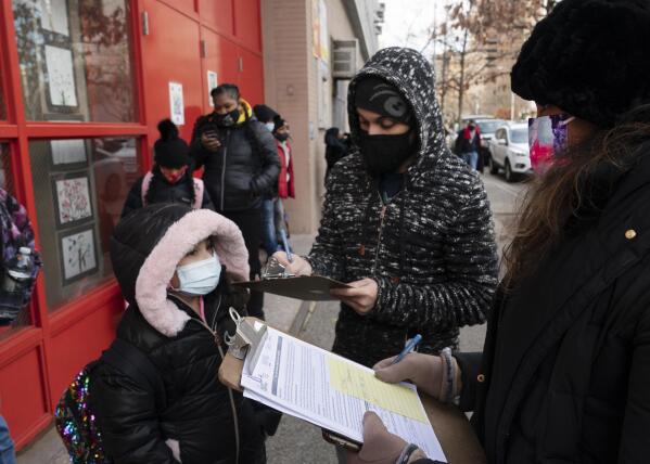FILE - In this Dec. 7, 2020, file photo, a parent, center, completes a form granting permission for random COVID-19 testing for students as he arrives with his daughter, left, at P.S. 134 Henrietta Szold Elementary School, in New York. Children are having their noses swabbed or saliva sampled at school to test for the coronavirus in cities such as Baltimore, New York and Chicago. As more children return to school buildings this spring, widely varying approaches have emerged on how and whether to test students and staff members for the virus. (AP Photo/Mark Lennihan, File)