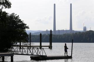 FILE - In this Aug. 7, 2019, file photo, a man fishes at William B. Ladd Park near the Kingston Fossil Plant in Kingston, Tenn. The head of America’s largest public utility says they are on track to reduce greenhouse gas emissions by 80% by the year 2035. Tennessee Valley Authority President and CEO Jeff Lyash made the remarks during an online event hosted by the Atlantic Council on Wednesday, April 28, 2021. (AP Photo/Mark Humphrey, File)
