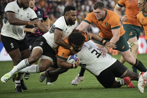 Australia's Zane Nonggorr, center, is tackled by Fiji's Luke Tagi during the Rugby World Cup Pool C match between Australia and Fiji at the Stade Geoffroy Guichard in Saint-Etienne, France, Sunday, Sept. 17, 2023. (AP Photo/Laurent Cipriani)