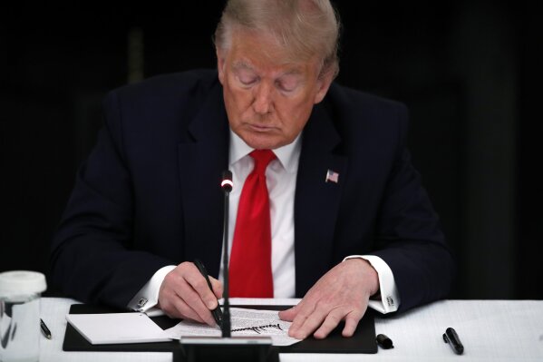 President Donald Trump signs his name on a piece of paper during a roundtable with governors on the reopening of America's small businesses, in the State Dining Room of the White House, Thursday, June 18, 2020, in Washington. (AP Photo/Alex Brandon)