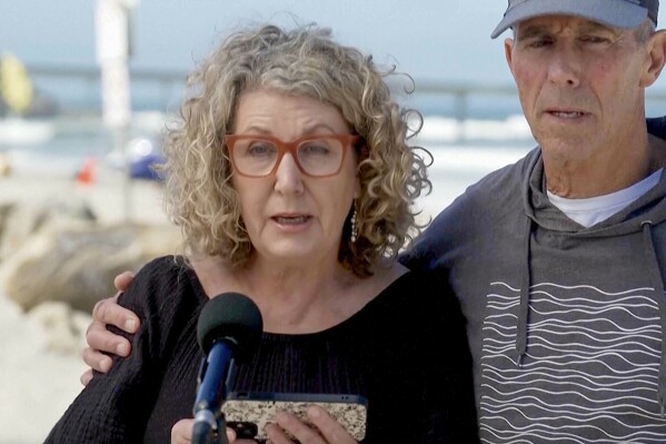 In this image taken from video, Australia's Debra Robinson with her husband Martin, address the media on the beach in San Diego, Tuesday, May 7, 2024 following the deaths in Mexico of their two sons during a surfing trip. The sons, Callum and Jake, and U.S. friend Jack Carter Rhoad, were allegedly killed by car thieves in Baja California, across the border from San Diego, somewhere around April 28 or 29. (Channel 9/POOL via AP)