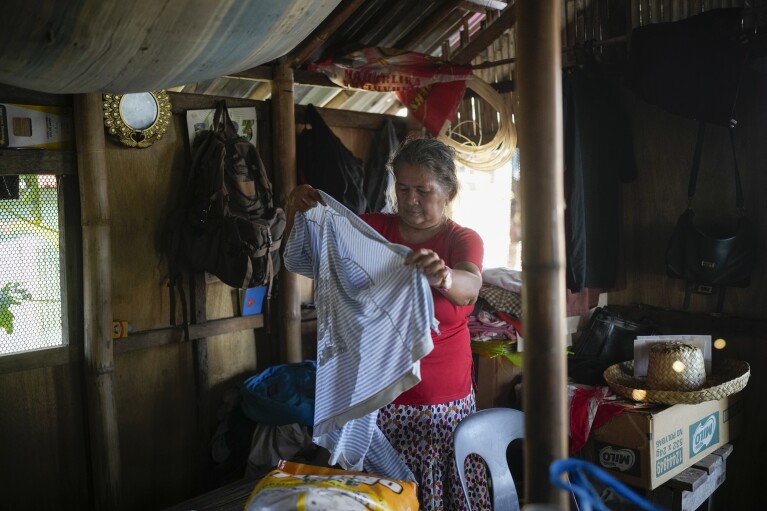 Wilma Abanil arranges clothes inside her house at the coastal village of Santa Clara near a liquified natural gas power plant in Batangas province, Philippines on Tuesday, Aug. 8, 2023. Abanil witnessed changes after the first plant opened in 2002. Within two years, the fish catch was falling, she said. It grew worse as more plants opened. (AP Photo/Aaron Favila)